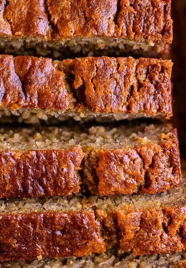 Slice of moist banana bread on a wooden board with ripe bananas