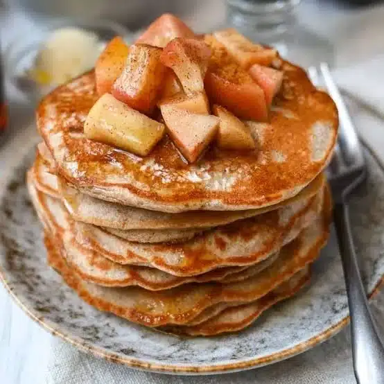 Fluffy apple cinnamon protein pancakes topped with fresh apples and cinnamon.