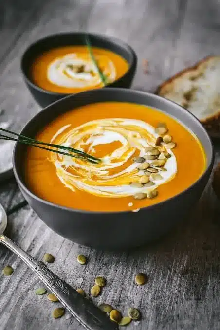 Bowl of creamy apple butternut squash soup garnished with herbs.