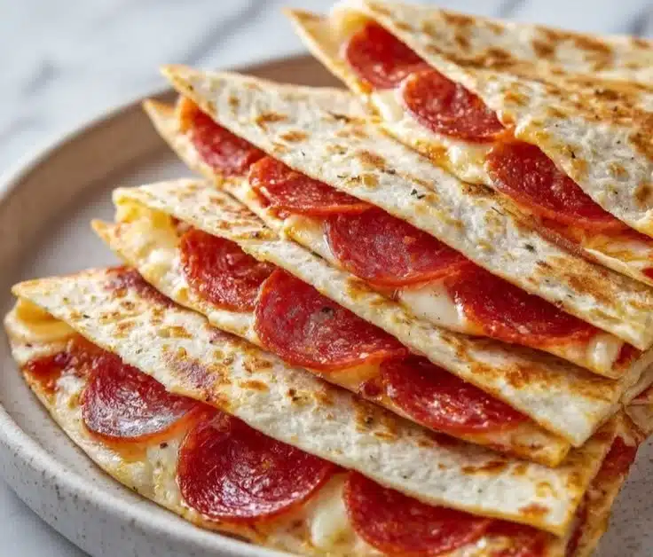 Pepperoni pizza quesadillas on a plate, garnished with herbs and dip.